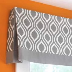 a window with a gray and white valance hanging from it's side next to an orange wall