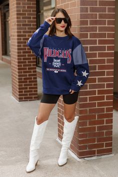 a woman standing in front of a brick wall wearing white boots and a blue sweatshirt