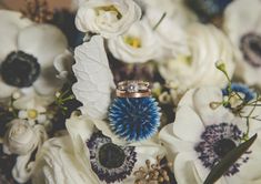 two wedding rings sitting on top of some white and blue flowers with greenery in the background