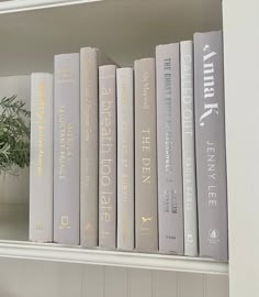 the books are lined up on the white book shelf next to a potted plant