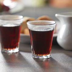 two shot glasses filled with liquid sitting on top of a wooden table next to bread