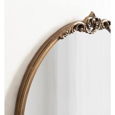 an ornate gold framed mirror against a white wall with the reflection of a flower on it