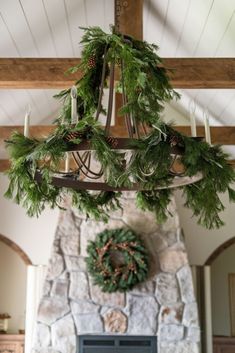 a chandelier hanging over a fireplace with evergreen wreaths and candles on it