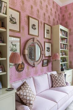 a living room with pink walls and pictures on the wall above the white couches