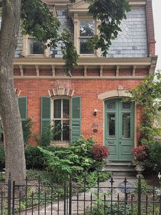 an old brick house with green shutters on the front and side doors, surrounded by trees