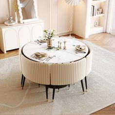 a living room with a round table surrounded by white chairs and tables in the middle