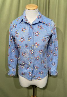 "This is a fun, vintage button front blouse from the 70s. Home sewn & beautifully made. The bust measures 32\", see measurements below. Made of a cotton blend in a blue denim look with flowers & strawberries. It has long sleeves, with quilted button cuffs. Collar is pointed and the front & back shoulders have a quilted western style yoke. It buttons all the way down the front. There are quilted patches on the elbows. The hemline is a straight hem. The blouse is in good condition! It is softly wo Fitted Spring Shirt With Snap Buttons, Fitted Shirt With Snap Buttons For Spring, Retro Tops With Vintage Pattern For Spring, Spring Cotton Blouse With Snap Buttons, Vintage Shirt For Spring Daywear, Vintage Shirt For Daywear In Spring, Spring Vintage Tops With Retro Print, Vintage Retro Print Tops For Spring, Collared Tops For Spring Vintage Fashion