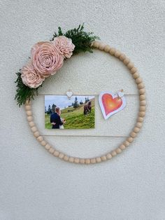 a photo frame with flowers and two photos hanging on the wall next to a flower wreath