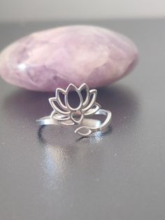 a silver lotus ring sitting on top of a rock next to a pink crystal stone