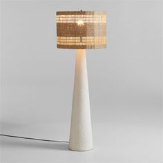 a white table lamp with a beige shade on it's side and a black cord plugged into the base