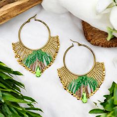 a pair of green and gold earrings on top of a white table next to flowers