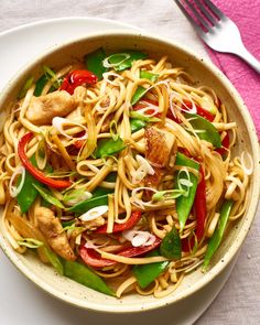 a bowl filled with noodles and vegetables on top of a table next to a fork