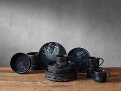 a wooden table topped with lots of black dishes and cups on top of each other