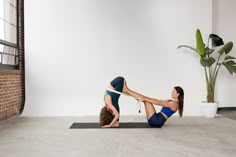 two women doing yoga exercises on mats in an empty room with a potted plant