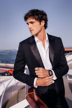 a man in a tuxedo standing on a boat looking at the camera with his hand on his hip