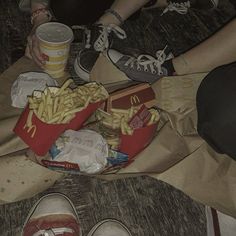 two people are sitting on the floor eating french fries and drinking soda while another person is standing next to them