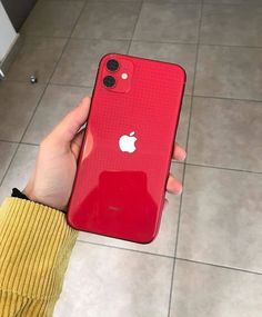 a person holding an apple phone in their hand on the tile floor next to a wall