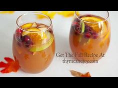 two glasses filled with drinks sitting next to each other on a white tablecloth and fall leaves