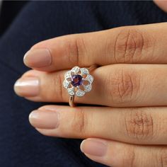 Sometimes when a girl says she likes to receive flowers as a gift, it's not the real flowers she meant. Think twice and go for the safest thing - our Flora ring with amethyst and side Moissanites. Floral jewelry is where it's at! Perfect as a graduation gift, birthday gift, anniversary ring, or a promise ring. Details: Center stone Gemstone: Amethyst Stone Shape: Round Measurements: 5.00mm Side stones Gemstone: Moissanite Shape: Round Measurements: 1.30mm (8) Band measurements: approx. 1.8mm wid Flower Shaped Proposal Ring, Wedding Flower Ring For Mother's Day, Mother's Day Wedding Flower Ring, Flower Shaped Diamond Ring Gift, Flower Shaped Purple Wedding Rings, Purple Flower-shaped Wedding Rings, Diamond Flower Ring With Halo Design For Gift, Diamond Flower Ring With Halo Design As Gift, Flower Shaped Rings With Rose Cut Diamonds For Gift