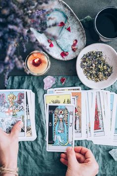 two hands holding tarot cards next to a bowl of flowers and a cup of tea