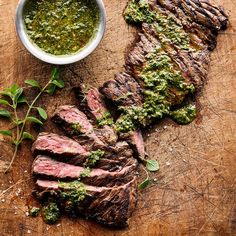 grilled steak with pesto sauce on wooden cutting board next to small bowl and sprig of basil