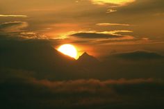 the sun is setting behind some clouds in the sky with mountains in the back ground