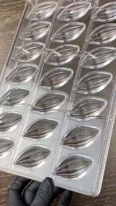 a hand holding a plastic tray filled with lots of silver metal discs on top of a wooden table