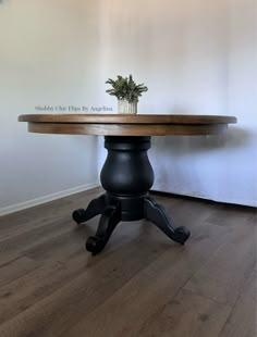 a small potted plant sits on top of a round wooden table with black legs