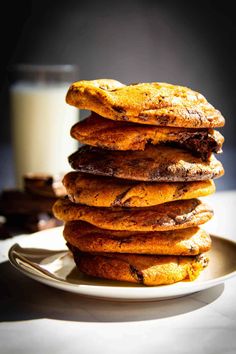 stack of chocolate chip cookies on a plate with a glass of milk in the background