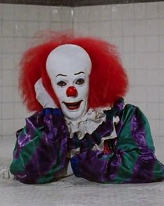 a creepy clown sitting on the ground with red hair