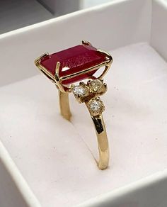 a gold ring with a red stone surrounded by three small diamonds in a white box