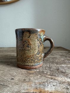 a brown and black coffee cup sitting on top of a wooden table next to a mirror