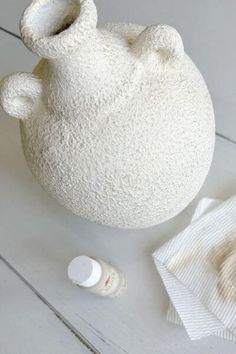 a white vase sitting on top of a wooden table next to a bottle and cloth