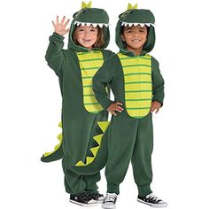 two children in dinosaur costumes standing next to each other, one holding his hand up