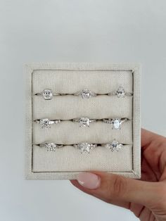 a hand holding a set of five rings in a white box with four different sized diamonds