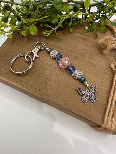 a keychain with a butterfly charm on it sitting next to some flowers and twine