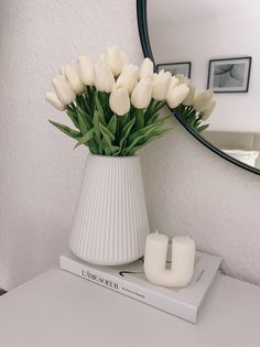 a white vase filled with flowers sitting on top of a table next to a mirror