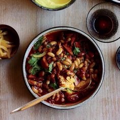 a bowl filled with beans and vegetables next to two glasses on a wooden counter top