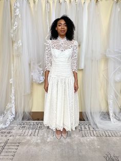 a woman standing in front of some wedding dresses hanging on a rack with white tulle