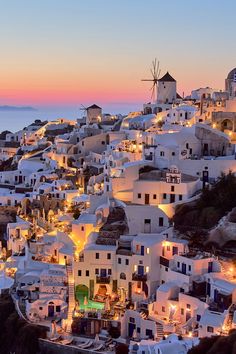 the white buildings are lit up at night on the hill side with windmills in the distance