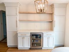 a kitchen with white cabinets and an open shelf above the wine cooler in the center