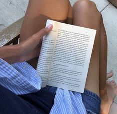 a person is reading a book while sitting on a wooden bench outside in the sun