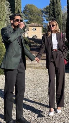 the man and woman are holding hands in front of some trees, one is wearing sunglasses