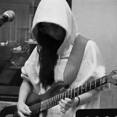 a person with long hair playing a guitar in front of a microphone and wearing a hood