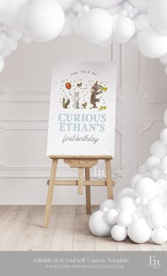 an easel with white balloons surrounding it and a sign that says curious ethan's first birthday