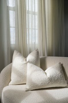 two white pillows sitting on top of a couch in front of a pair of windows