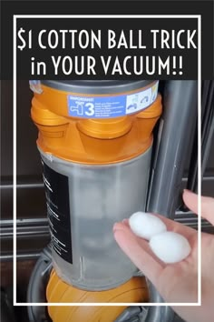 a person is holding two white balls in front of a yellow and gray vacuum cleaner