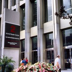 people are walking in front of the world trade center building with flowers on display outside