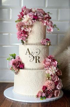 a three tiered wedding cake with pink flowers on the top and initials on the side