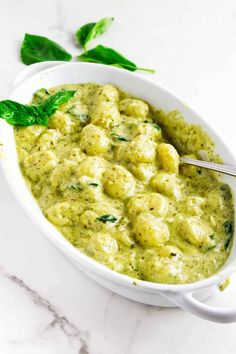 a white bowl filled with green food and garnished with basil on the side